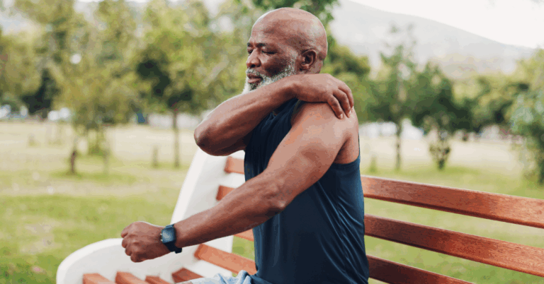 Does Microwaving Food Cause Cancer? 1 Older Black man sitting on a bench in a park, clutching his left shoulder with his right hand, likely due to pain from lung cancer