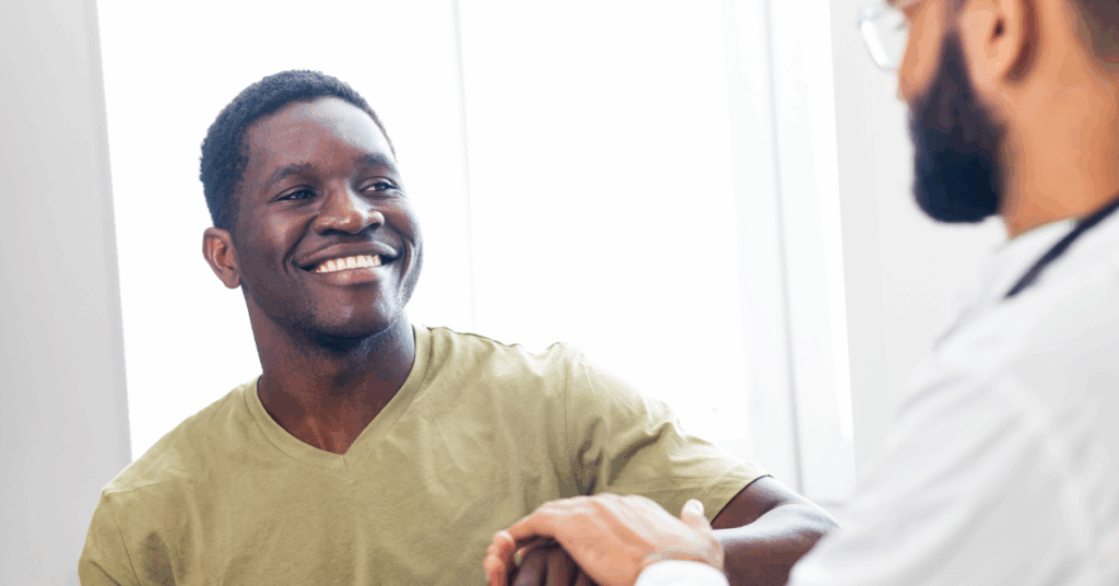 General Wellness 8 Young African American man smiling and shaking a doctor’s hand during prostate cancer screening.