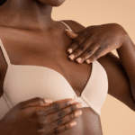 Close-up of an African American woman’s torso. She’s wearing a pink bra and performing a self-exam to check for signs of breast cancer