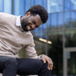 Young Black man sitting on a bench in pain, with his right hand clutching his back as he may have CKD