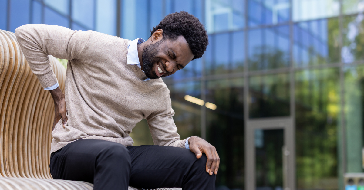 Young Black man sitting on a bench in pain, with his right hand clutching his back as he may have CKD