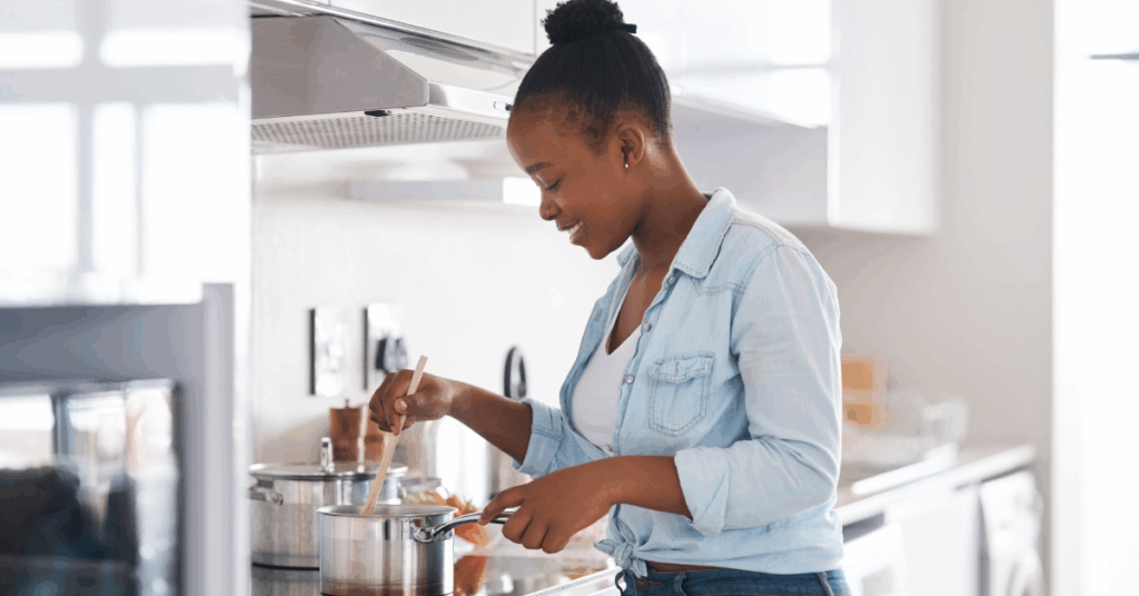 Young Black woman stirring a pot on a stove in the kitchen, using alternatives to salt to season her food to reduce risk of heart failure