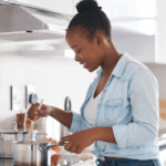 Young Black woman stirring a pot on a stove in the kitchen, using alternatives to salt to season her food to reduce risk of heart failure