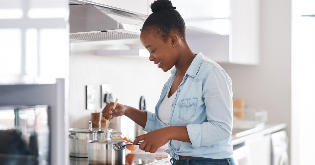 Young Black woman stirring a pot on a stove in the kitchen, using alternatives to salt to season her food to reduce risk of heart failure