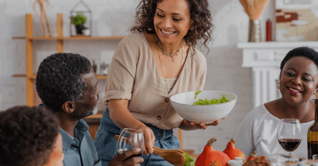 African American woman using tongs to serve salad to family and son during a Thanksgiving celebration