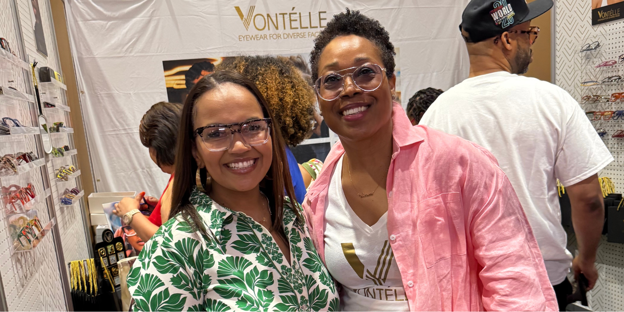 Tiffany Whitlow, co-founder and CDO, Acclinate, and Tracy Vontélle Green, Co-Founder and CEO of Vontélle Eyewear, wearing glasses standing in front of a white banner at Vontélle Eyewears’ vendor booth.