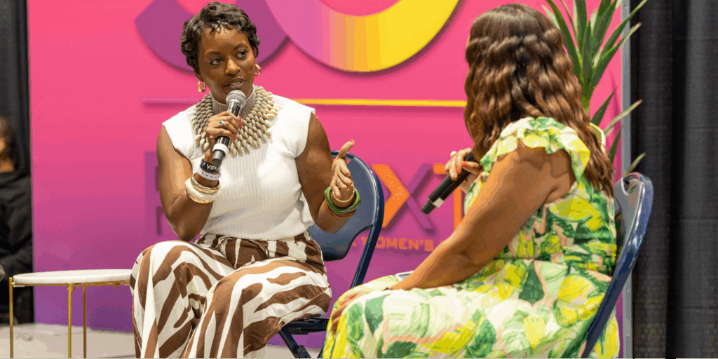Victoria Tyler and Tiffany Whitlow, co-founder and CDO, Acclinate, sit on a stage, participate in a panel discussion in front of a pink and yellow branded background at the Black Women’s Expo.
