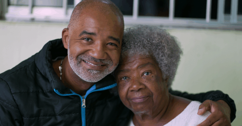 A Black adult son hugging senior Black mother, who may have Alzheimer’s