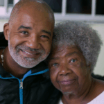 A Black adult son hugging senior Black mother, who may have Alzheimer’s