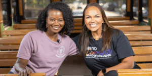 Michelle Brantley-Smith, founder of The Good Root Grove Co., and Tiffany Whitlow, Co-founder and CDO, Acclinate smiling together while sitting on a wooden trolley.