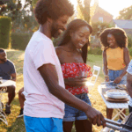 Black couple grilling red meat skewers, which increases risk of prostate cancer, at a multi-generation family barbecue.