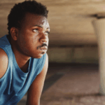 Black man in a blue tanktop, sweating and out of breath, potentially due to heart failure