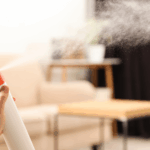 Close-up of a hand holding an air freshener can and spraying their living room