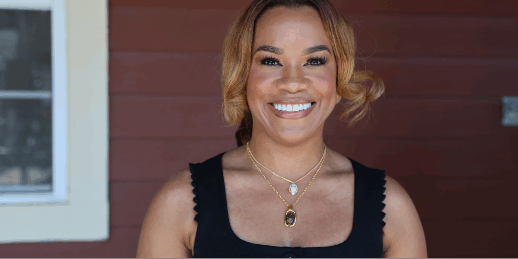 Quench Hydration founder and ER nurse, Alma Austin, stands outdoors against a brown wooden wall.
