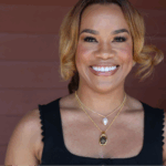 Quench Hydration founder and ER nurse, Alma Austin, stands outdoors against a brown wooden wall.