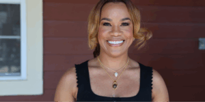 Quench Hydration founder and ER nurse, Alma Austin, stands outdoors against a brown wooden wall.