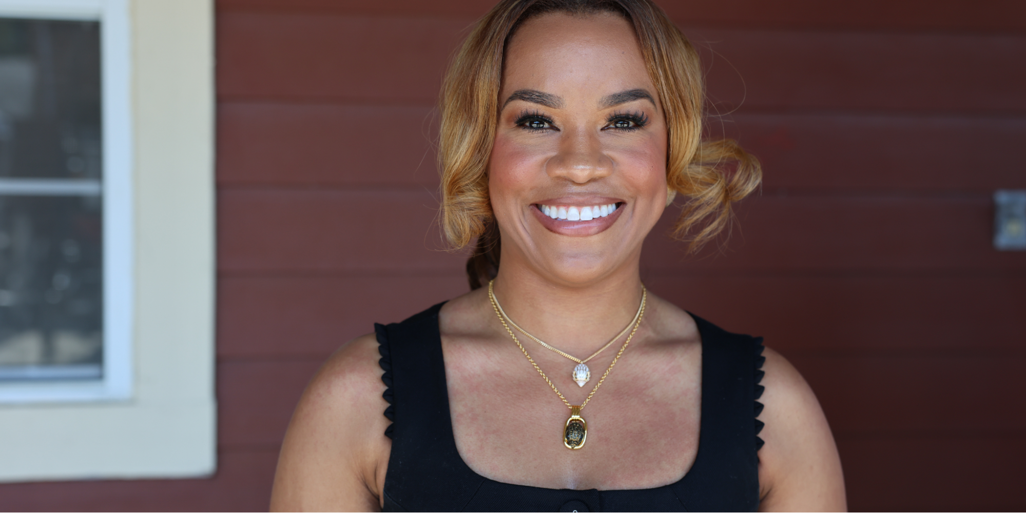Quench Hydration founder and ER nurse, Alma Austin, stands outdoors against a brown wooden wall.