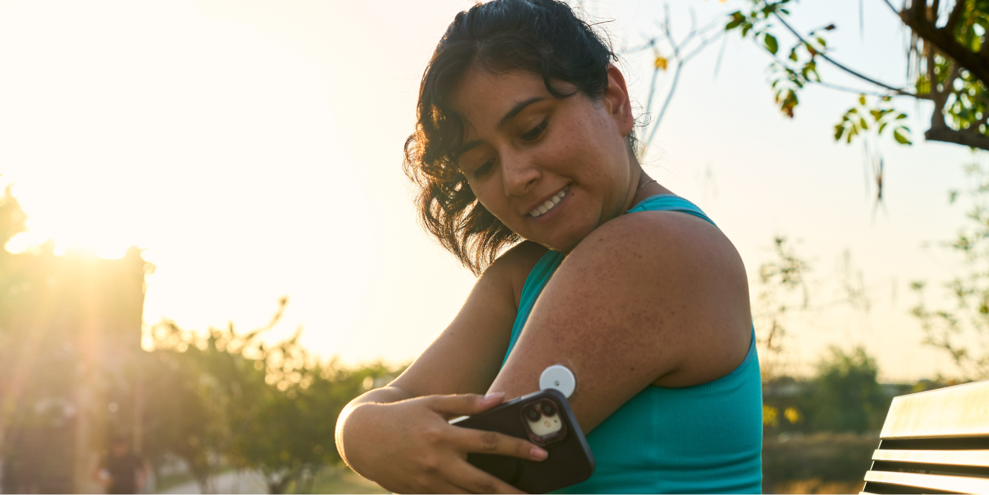 A close-up of a Hispanic woman in athletic wear managing her health by using a Continuous Glucose Monitor (CGM) attached to her arm.
