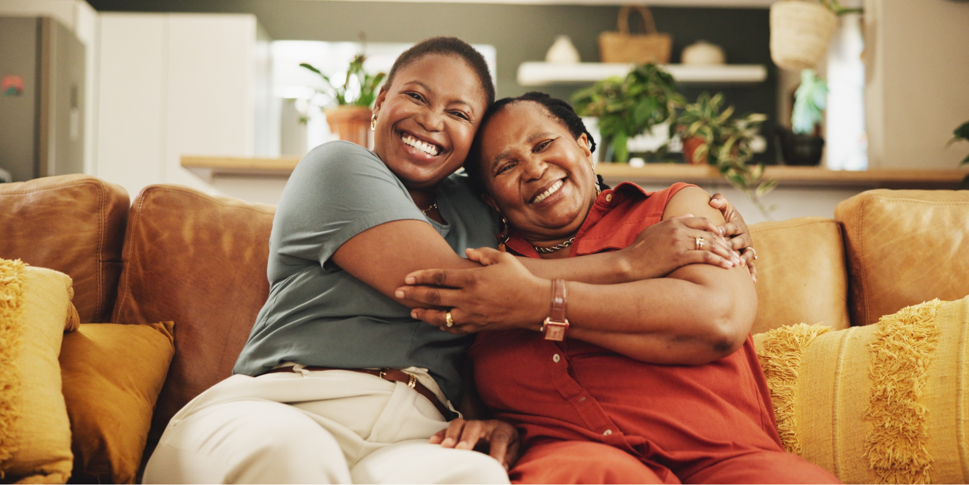 A close-up of two Black women smiling and embracing at home, highlighting the importance of shared health awareness to lower your breast cancer risk.