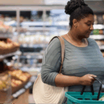 A Black woman making a healthy food swap to lower blood pressure by carefully checking the label on a bottle of juice at the grocery store.
