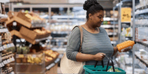 A Black woman making a healthy food swap to lower blood pressure by carefully checking the label on a bottle of juice at the grocery store.
