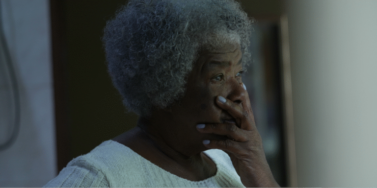 How to Talk to Your Kids About Cancer 1 A Black elderly woman looking out a window appearing troubled by memory loss caused by normal aging or dementia.