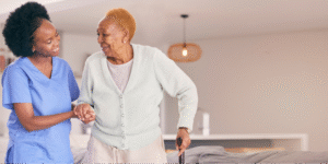 A caregiver smiling while helping a Black senior woman walk, highlighting the role of supportive care when navigating questions about lung cancer.
