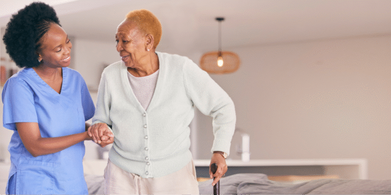 A caregiver smiling while helping a Black senior woman walk, highlighting the role of supportive care when navigating questions about lung cancer.