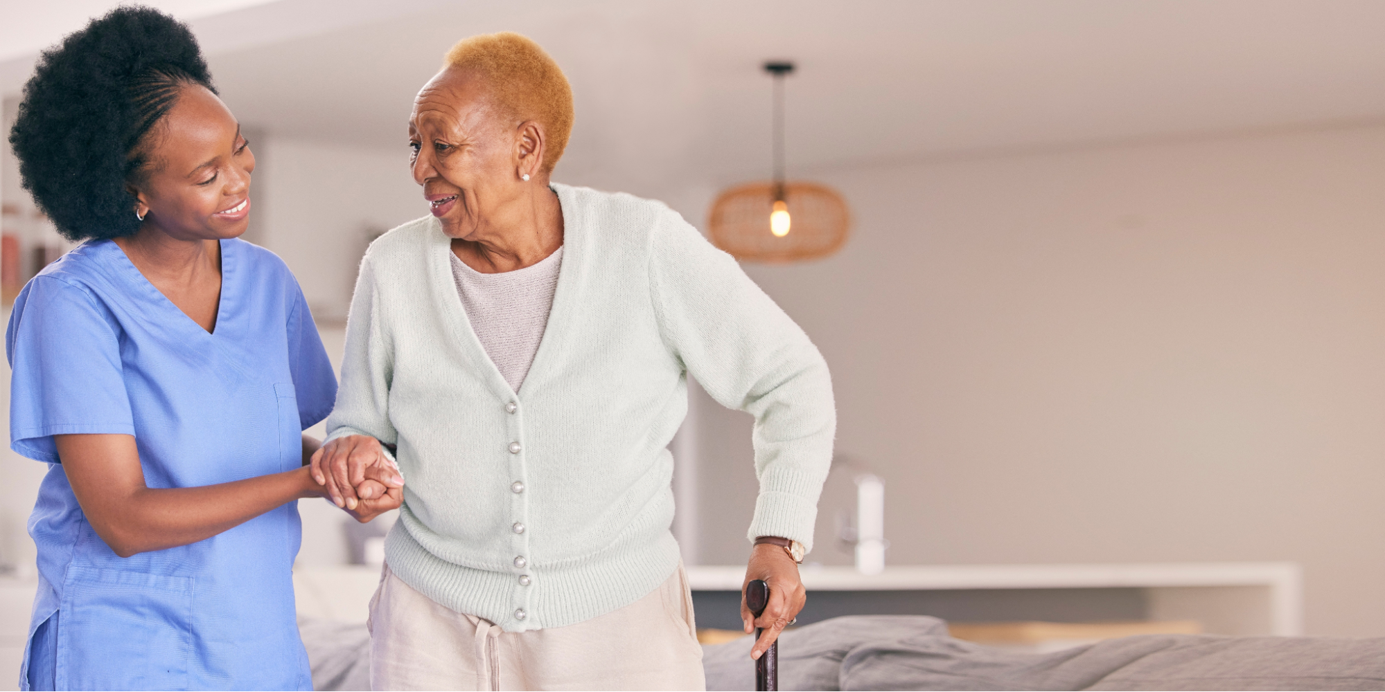 A caregiver smiling while helping a Black senior woman walk, highlighting the role of supportive care when navigating questions about lung cancer.