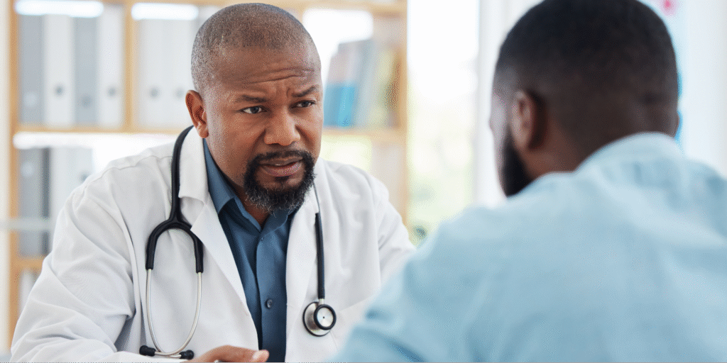 A close-up of a Black doctor and Black male patient discussing watchful waiting as a treatment option for prostate cancer.