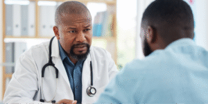 A close-up of a Black doctor and Black male patient discussing watchful waiting as a treatment option for prostate cancer.