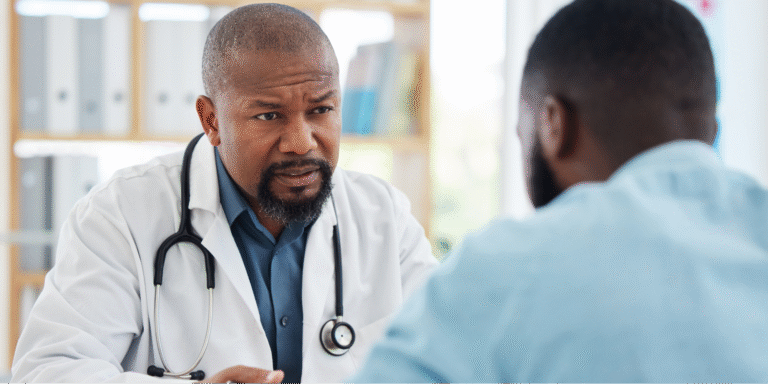 A close-up of a Black doctor and Black male patient discussing watchful waiting as a treatment option for prostate cancer.