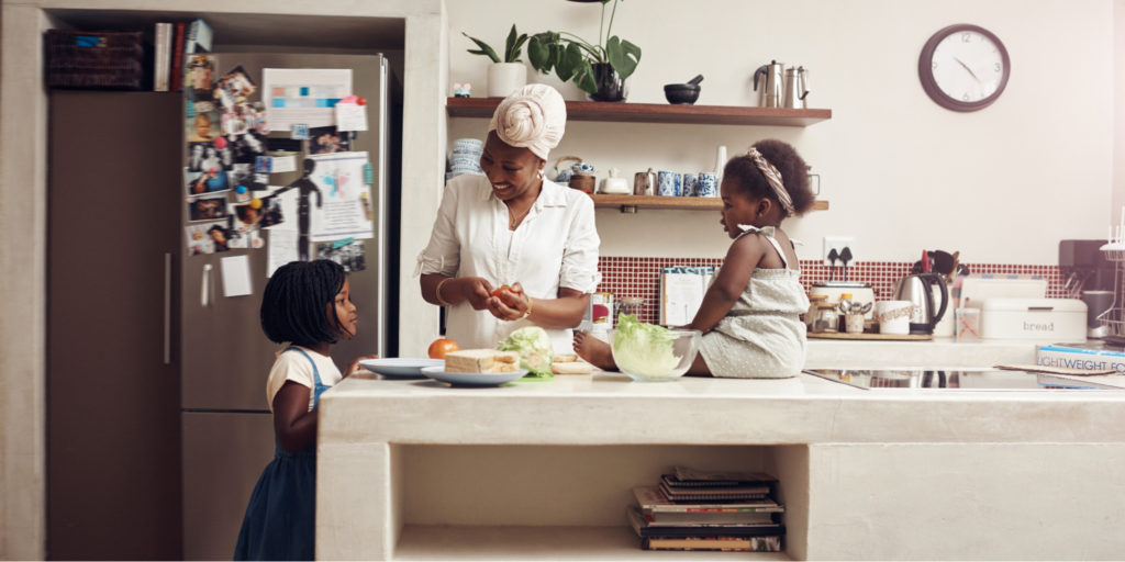 A Black mother with breast cancer preparing a chemo friendly meal with her two young daughters in their home kitchen.