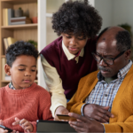Black father sitting on a couch with his two sons, looking at his laptop to learn more about if lung cancer is hereditary.