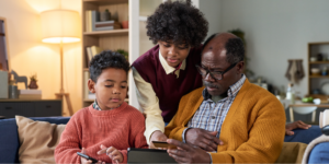 Black father sitting on a couch with his two sons, looking at his laptop to learn more about if lung cancer is hereditary.