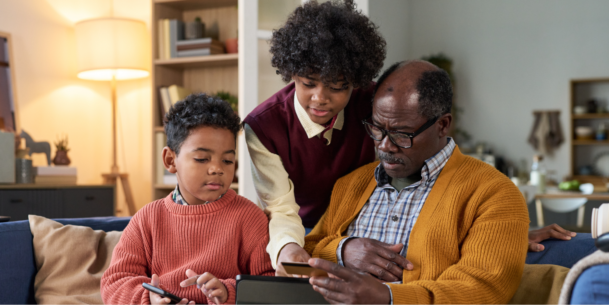 Black father sitting on a couch with his two sons, looking at his laptop to learn more about if lung cancer is hereditary.