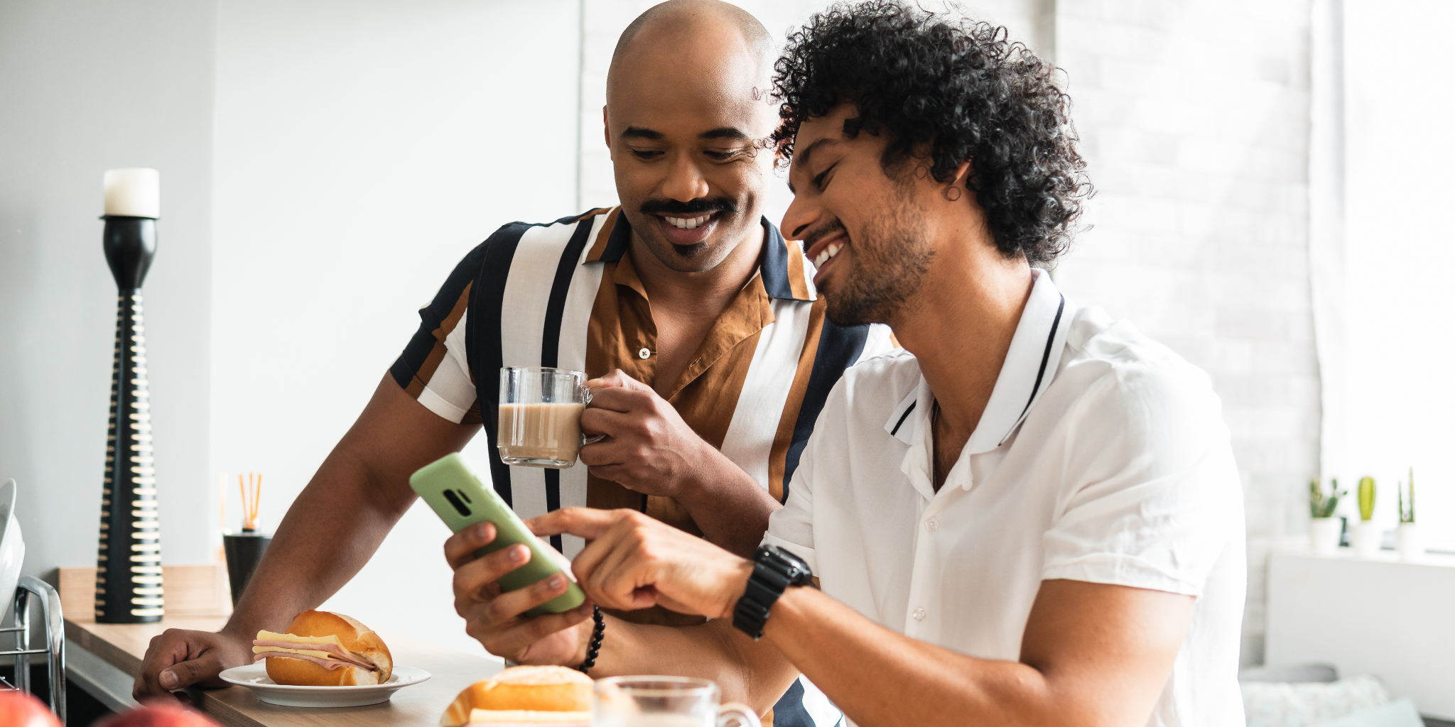 Two young Black men in collared shirts drinking coffee and eating breakfast while reading an article about hidden sugars and fat on a cell phone.