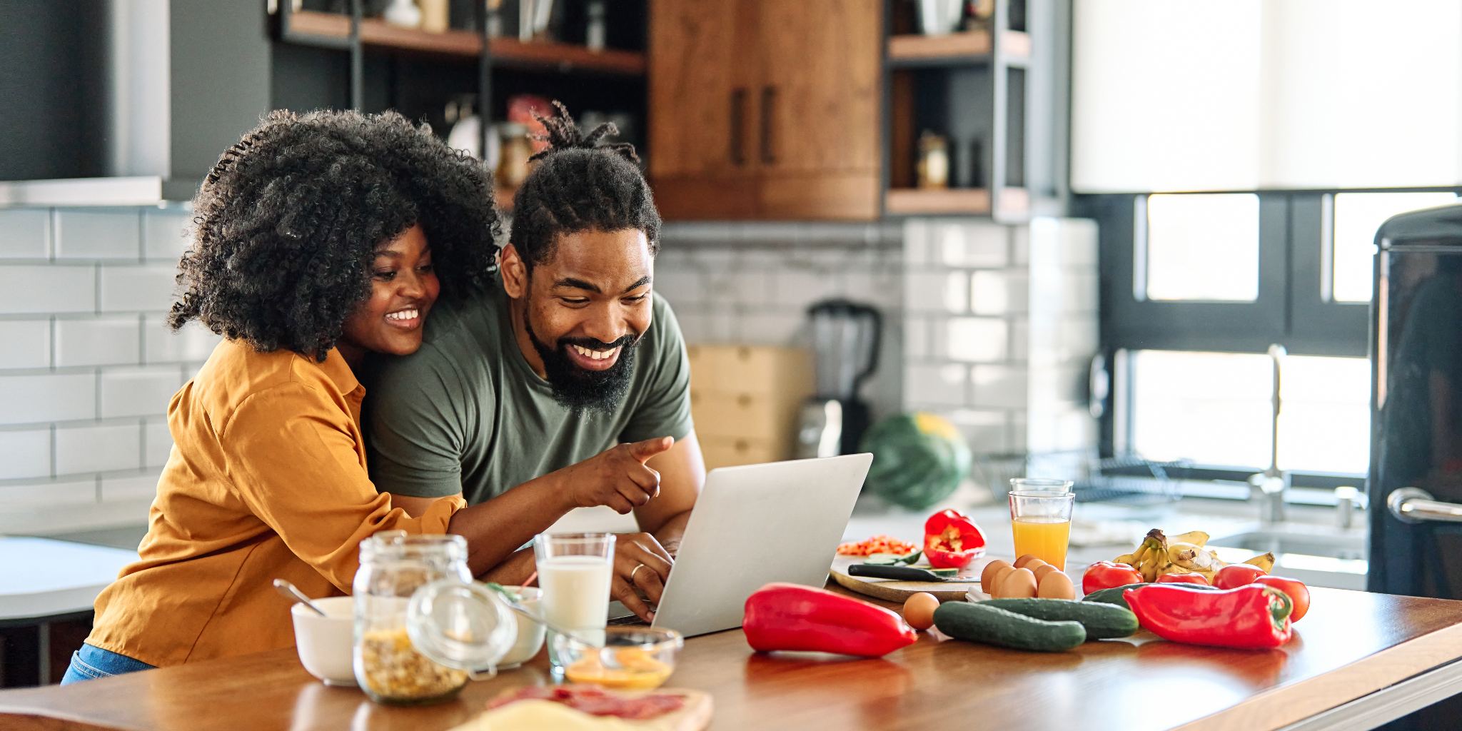 Young Black couple leaning over kitchen counter, looking for cheap magnesium foods online using a laptop.