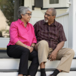 Older Black couple sitting outside on their porch step, smiling and talking about ways to protect your memory, especially in old age