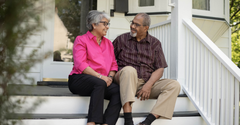 Older Black couple sitting outside on their porch step, smiling and talking about ways to protect your memory, especially in old age