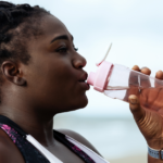 Side profile of a middle-aged Black woman drinking out of a pink water bottle, to maintain hydration with chronic kidney disease