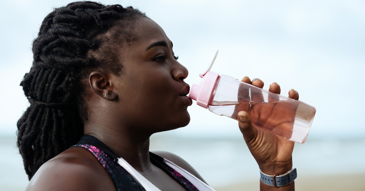 Side profile of a middle-aged Black woman drinking out of a pink water bottle, to maintain hydration with chronic kidney disease
