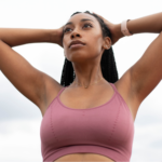 Confident young Black woman with her hands on her head in a pink sports bra, modeling one of the best bras for breast cancer survivors