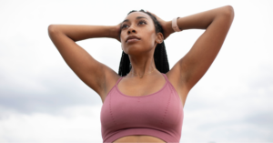 Confident young Black woman with her hands on her head in a pink sports bra, modeling one of the best bras for breast cancer survivors