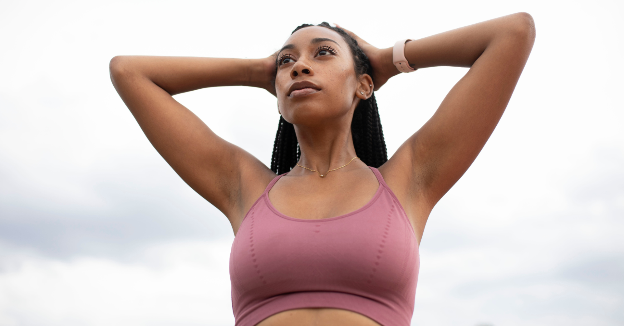 Confident young Black woman with her hands on her head in a pink sports bra, modeling one of the best bras for breast cancer survivors
