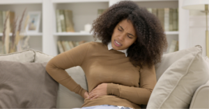 Young Black woman sitting on the couch in pain holding her right side due to back pain, one of the lung cancer symptoms in women