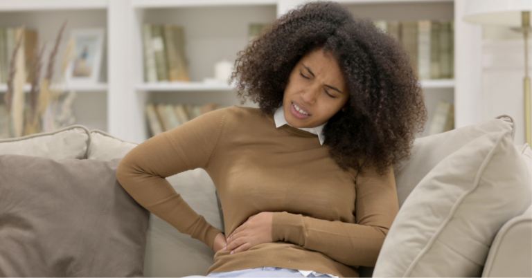 5 Websites To Help You Find the Right Therapist 1 Young Black woman sitting on the couch in pain holding her right side due to back pain, one of the lung cancer symptoms in women
