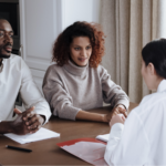 Black couple in their mid-30s sitting at a table with pen and paper listening to a health care professional explain the stages of prostate cancer
