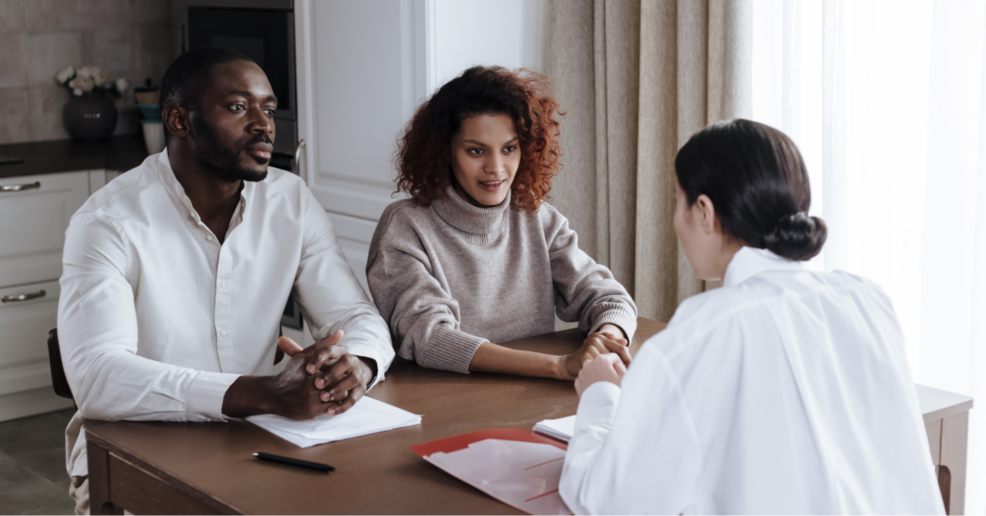 Black couple in their mid-30s sitting at a table with pen and paper listening to a health care professional explain the stages of prostate cancer