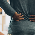 A close-up image of a person clutching their lower back, an early warning sign of where lung cancer spreads in the body.
